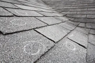 Close-up of gray asphalt roof shingles with white chalk circles marking damage from hailstorm. The image conveys a need for roof repair.
