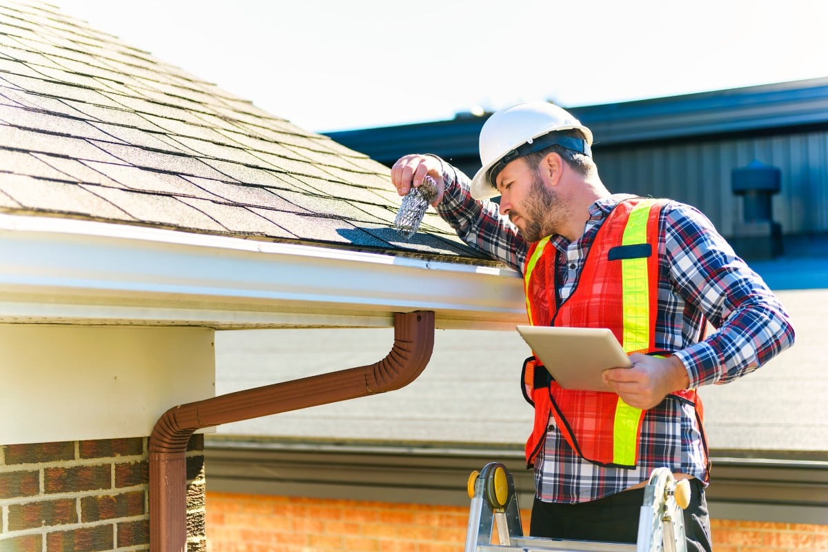 A man with hard hat standing on steps inspecting house roof